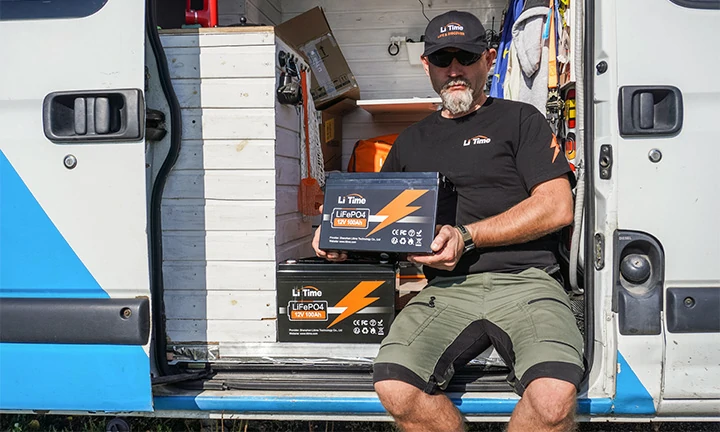 a man sits in the side doorway of his van, holding a LiTime 12V 100Ah LiFePO4 battery with another one visible inside