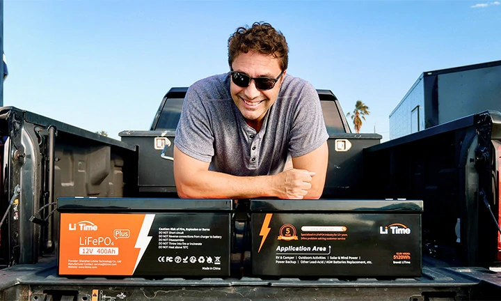 A man stands proudly behind two large LiTime batteries, including a 12V 400Ah model, ready for off-grid power in his truck