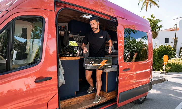 a man in a LiTime shirt carries a large LiFePO4 battery into his custom-built camper van, ready for an off-grid adventure