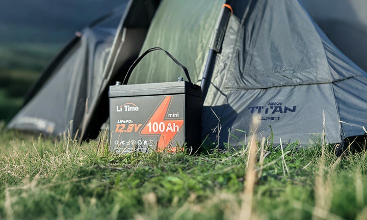 a portable LiTime mini 12.8V 100Ah battery sits in the grass at a campsite, ready to provide off-grid power for a tent