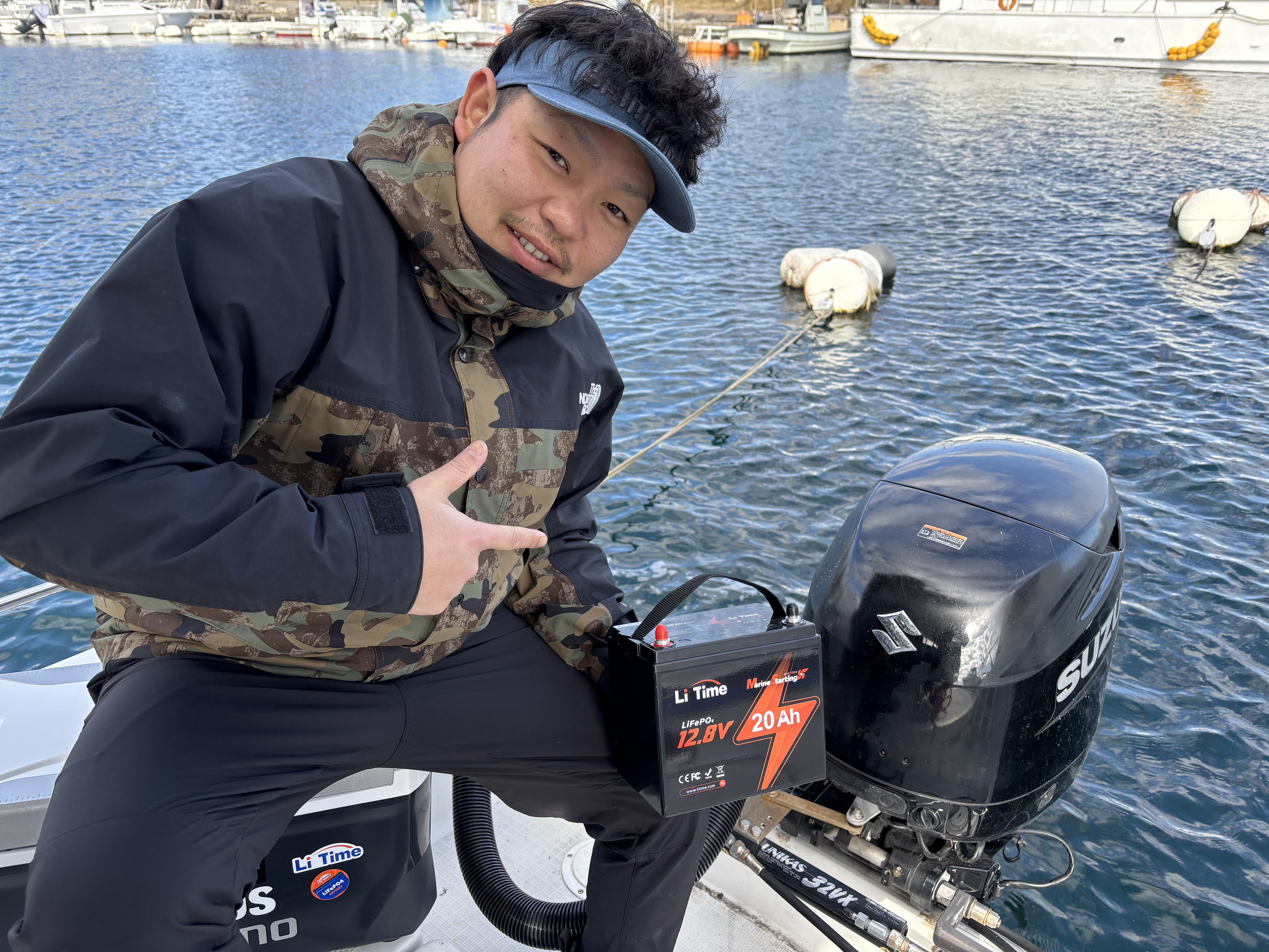 A customer on his boat holds the LiTime 12V 20Ah marine starting battery next to the outboard motor