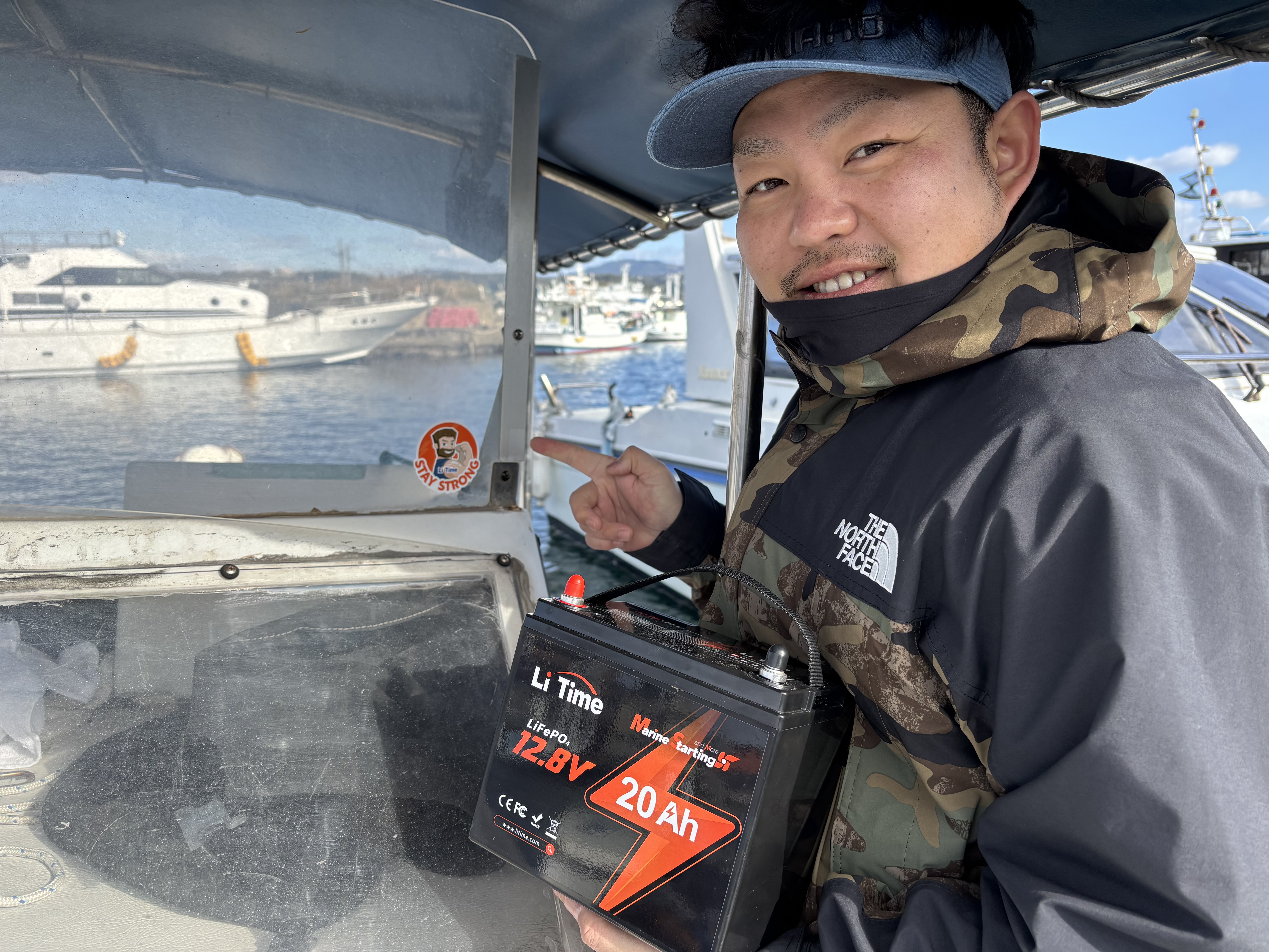 A smiling boater proudly points to his new LiTime 12V 20Ah marine starting battery inside the boat's cockpit