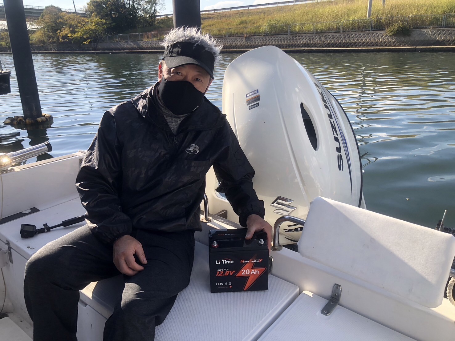 A boater sits next to his outboard motor with the LiTime 12V 20Ah marine starting battery on the deck.