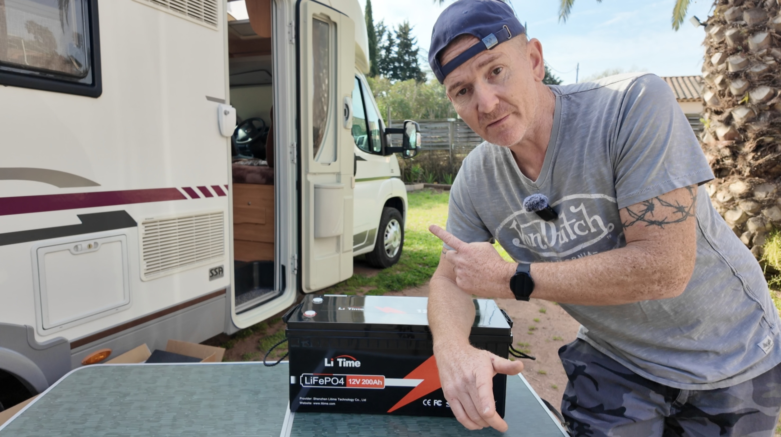 A man standing next to his large motorhome, proudly pointing to a new LiTime 12V 200ah lithium battery on a table