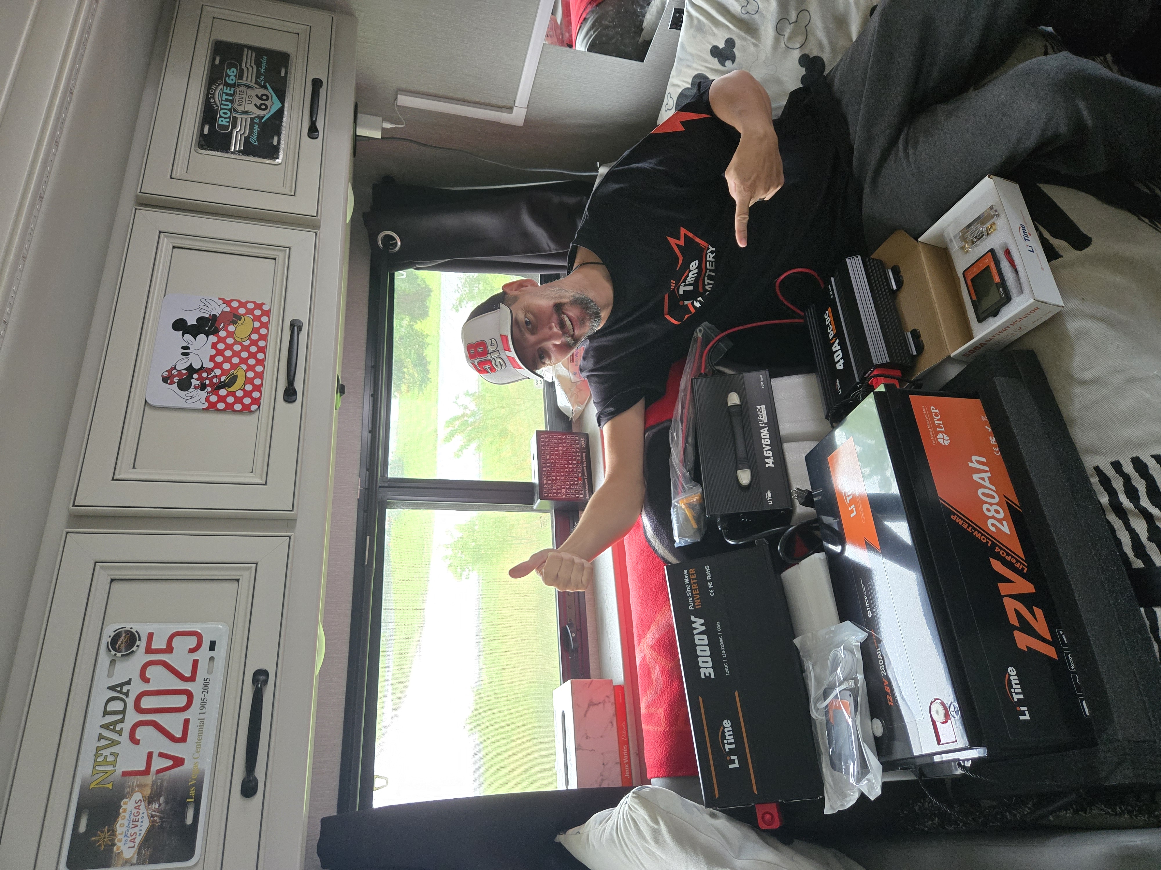A man sitting on a camper van bed surrounded by multiple LiTime 12V lithium batteries, giving a thumbs-up