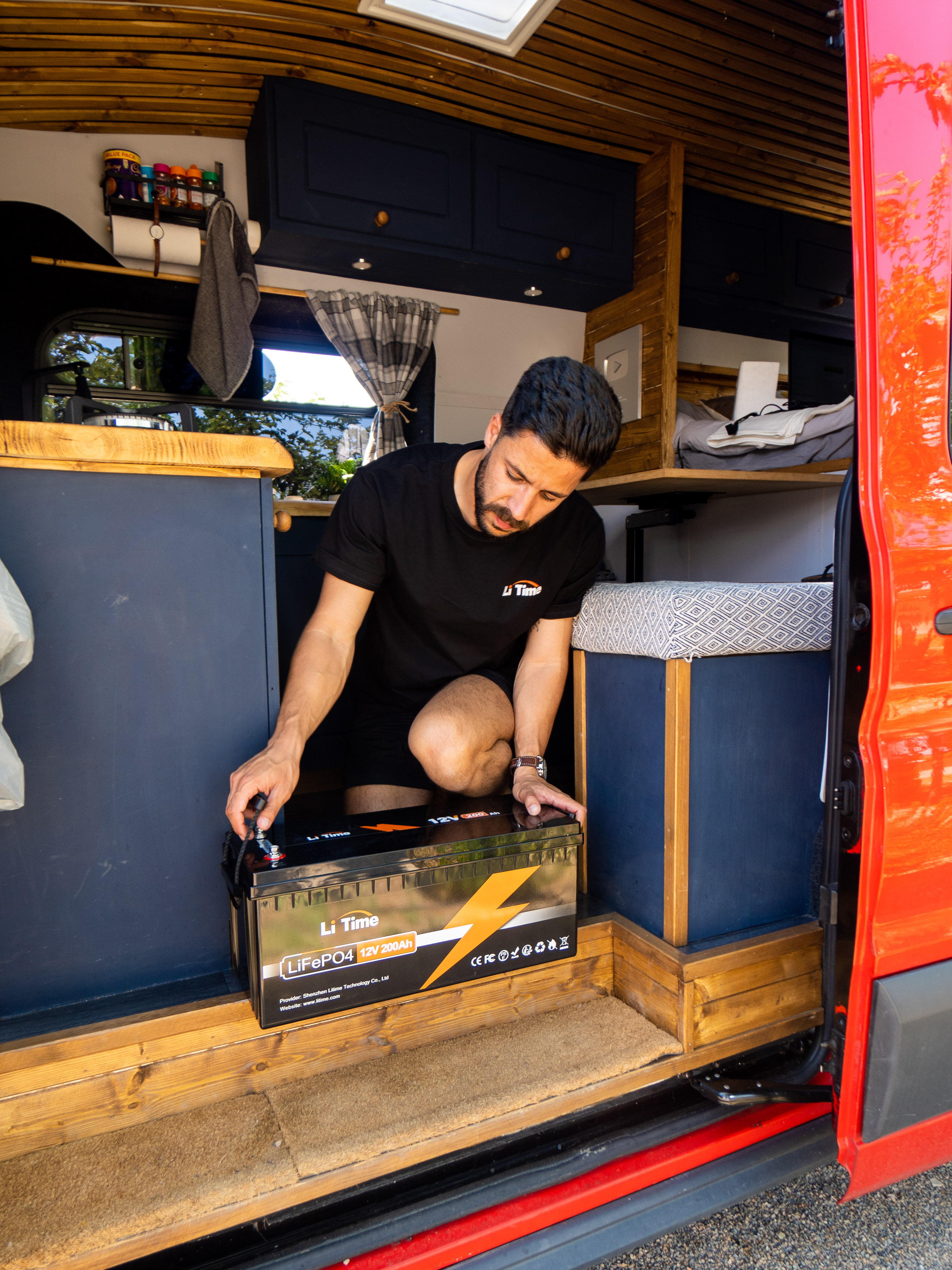 customer carefully placing a new LiTime 12V battery inside their camper van, preparing for installation or storage