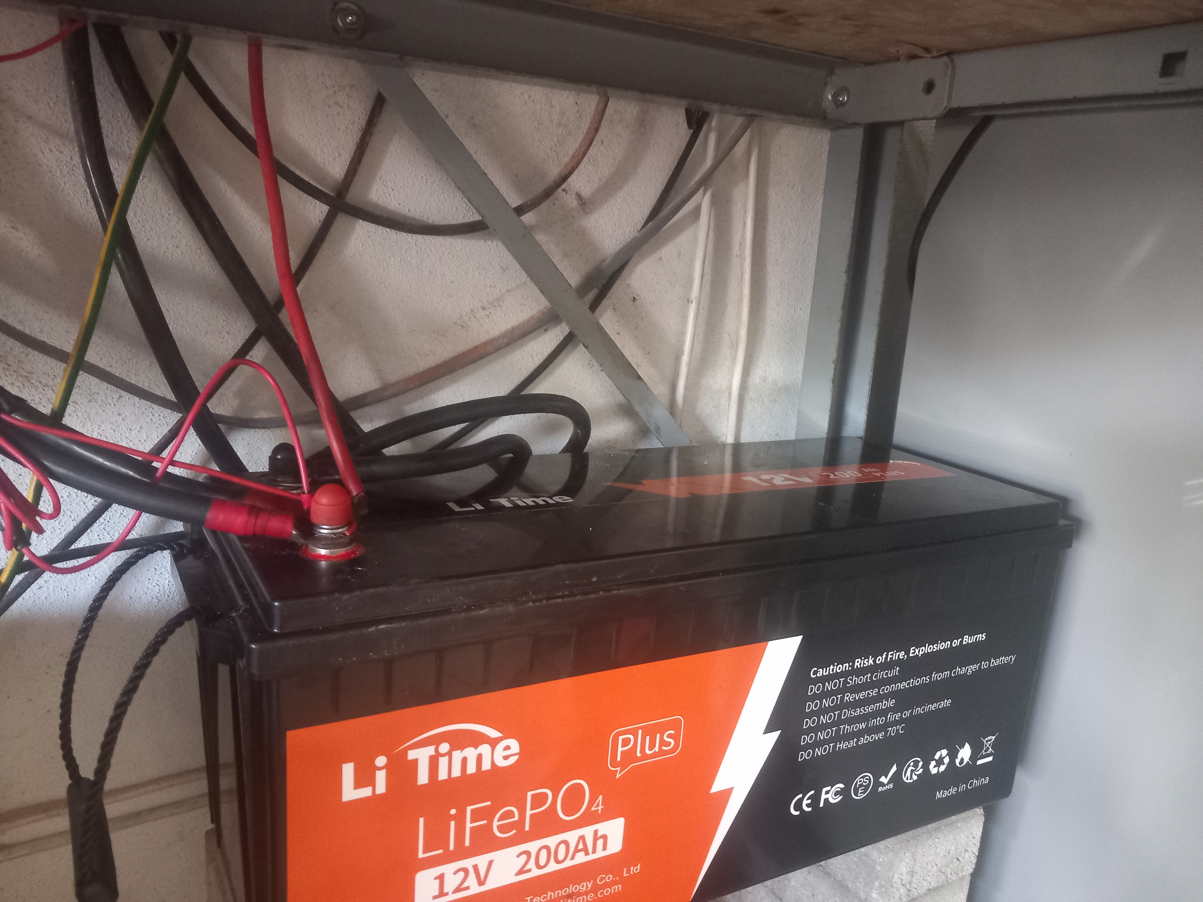  A close-up view of a LiTime 12V lithium battery installed inside a camper van, showing the wiring connections and the battery label